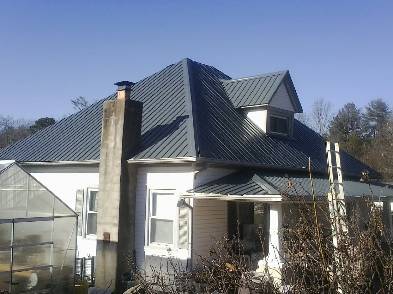 Dark blue standing seam metal roof on a white farmhouse with dormer — Slate & Tile Roof Repair by Roofing Brothers in Islip Terrace