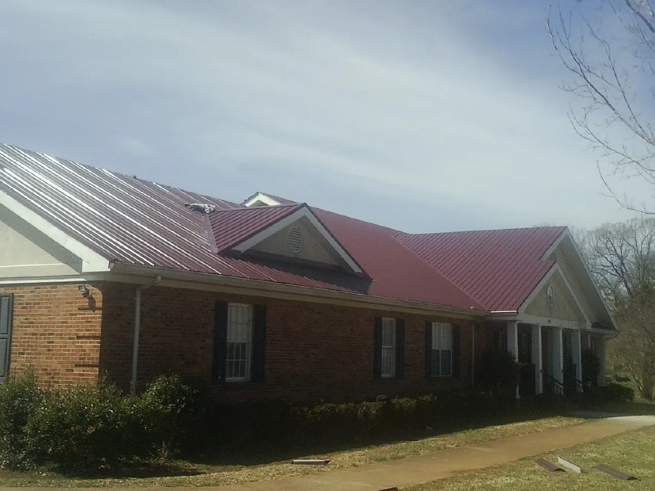 Red metal roof with gabled entries on a long brick building, from a Hail Damage Roof Repair job in Islip Terrace