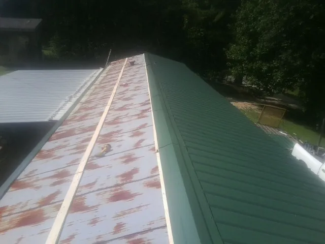 Old rusted panels beside newly installed green metal roofing — Wind Damage Roof Repair by Roofing Brothers in Islip Terrace
