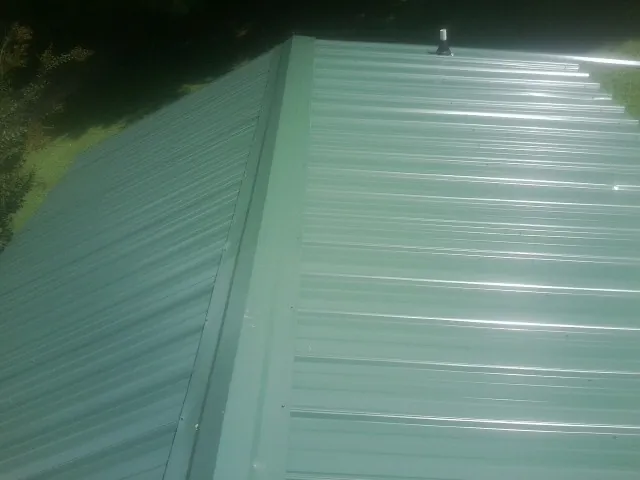 New green metal panels meeting at the ridge of a roof — Flat Roof Repair work by our crew in Islip Terrace