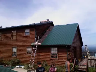 Green metal roof going on a two story log home with ladders set in Islip Terrace