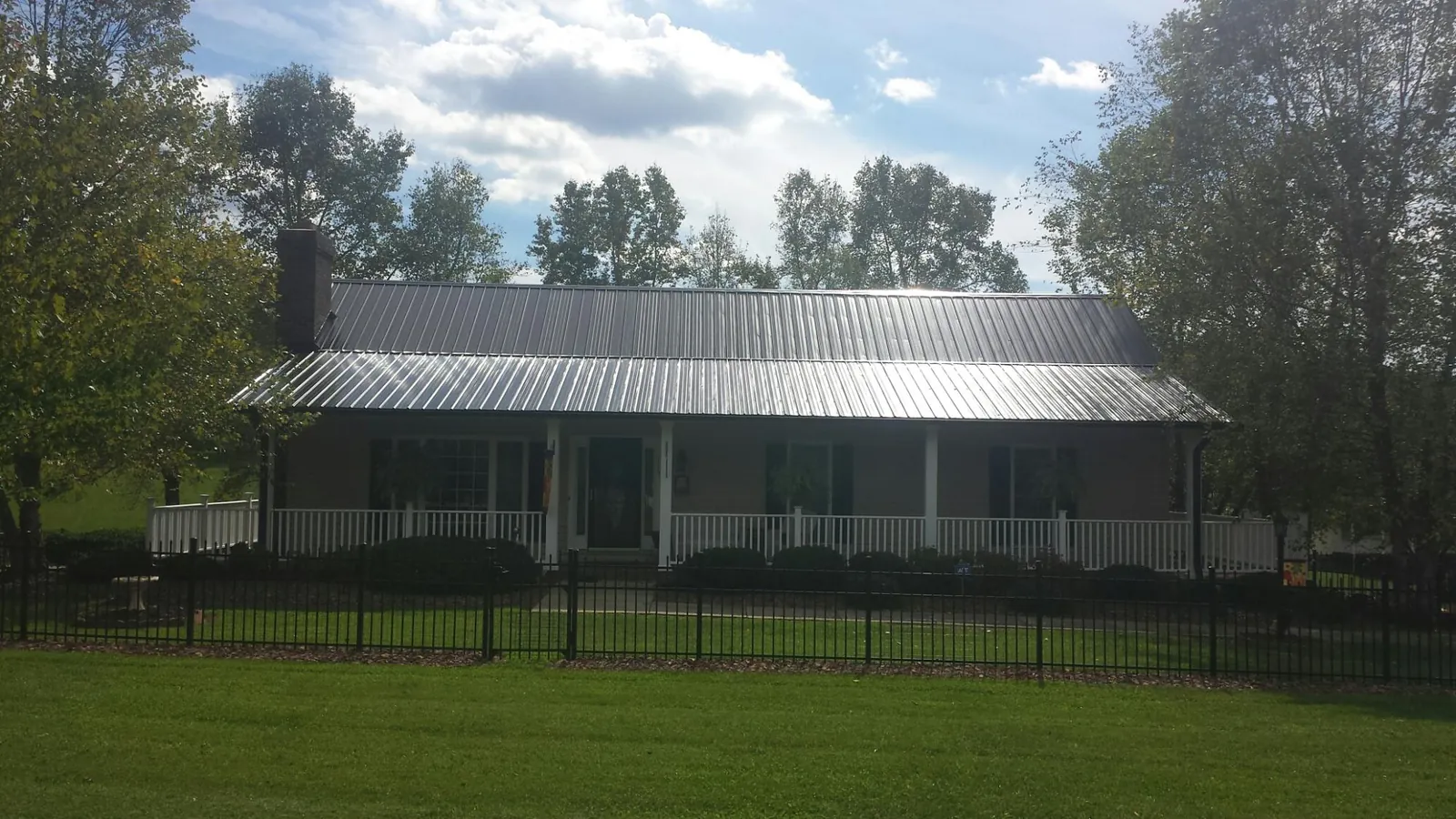 Gray metal roof on a brick ranch with a full width front porch — Gutter Guard Installation work by our crew in Islip Terrace