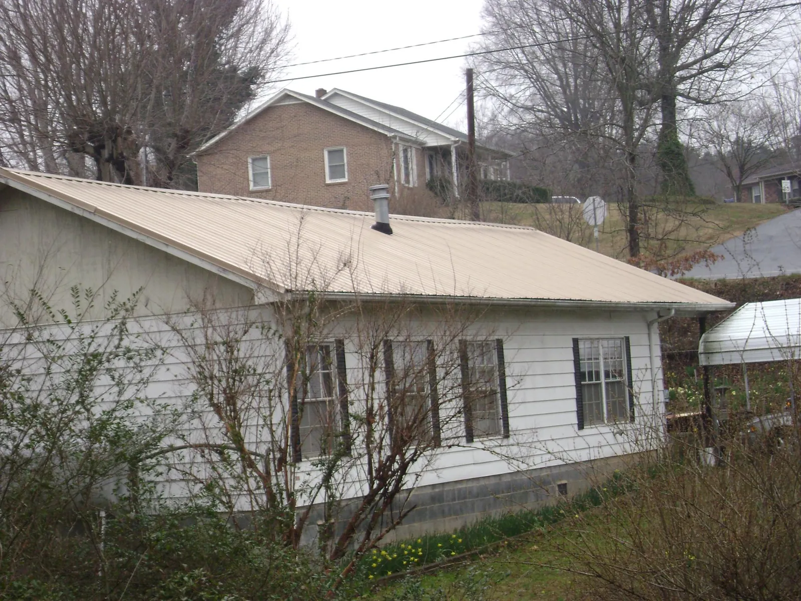Tan metal roof on a white sided house set into a hillside — Commercial Roofing by Roofing Brothers in Islip Terrace