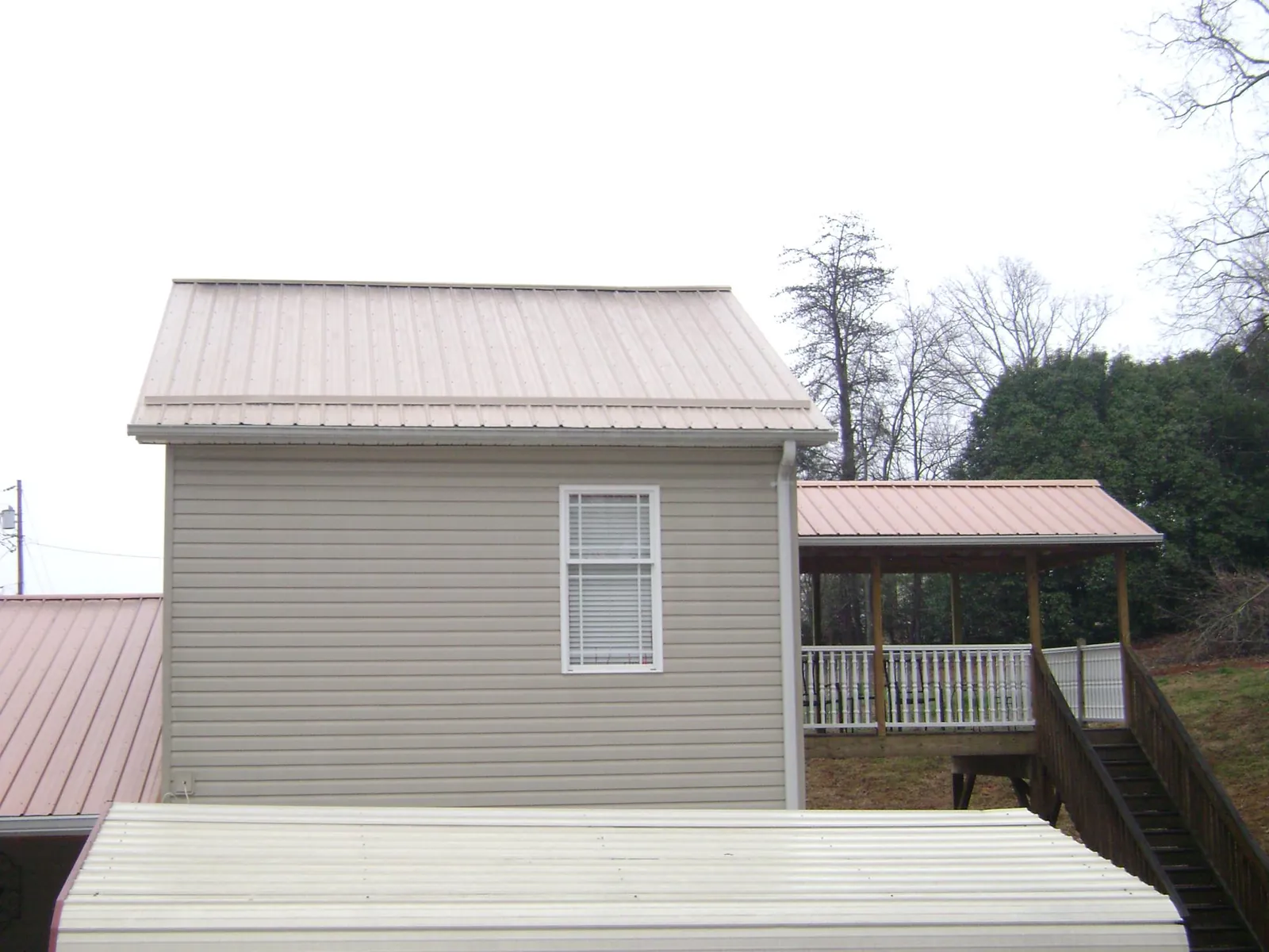 Tan metal roofs on a two story addition and attached porch, from a Roof Replacement job in Islip Terrace
