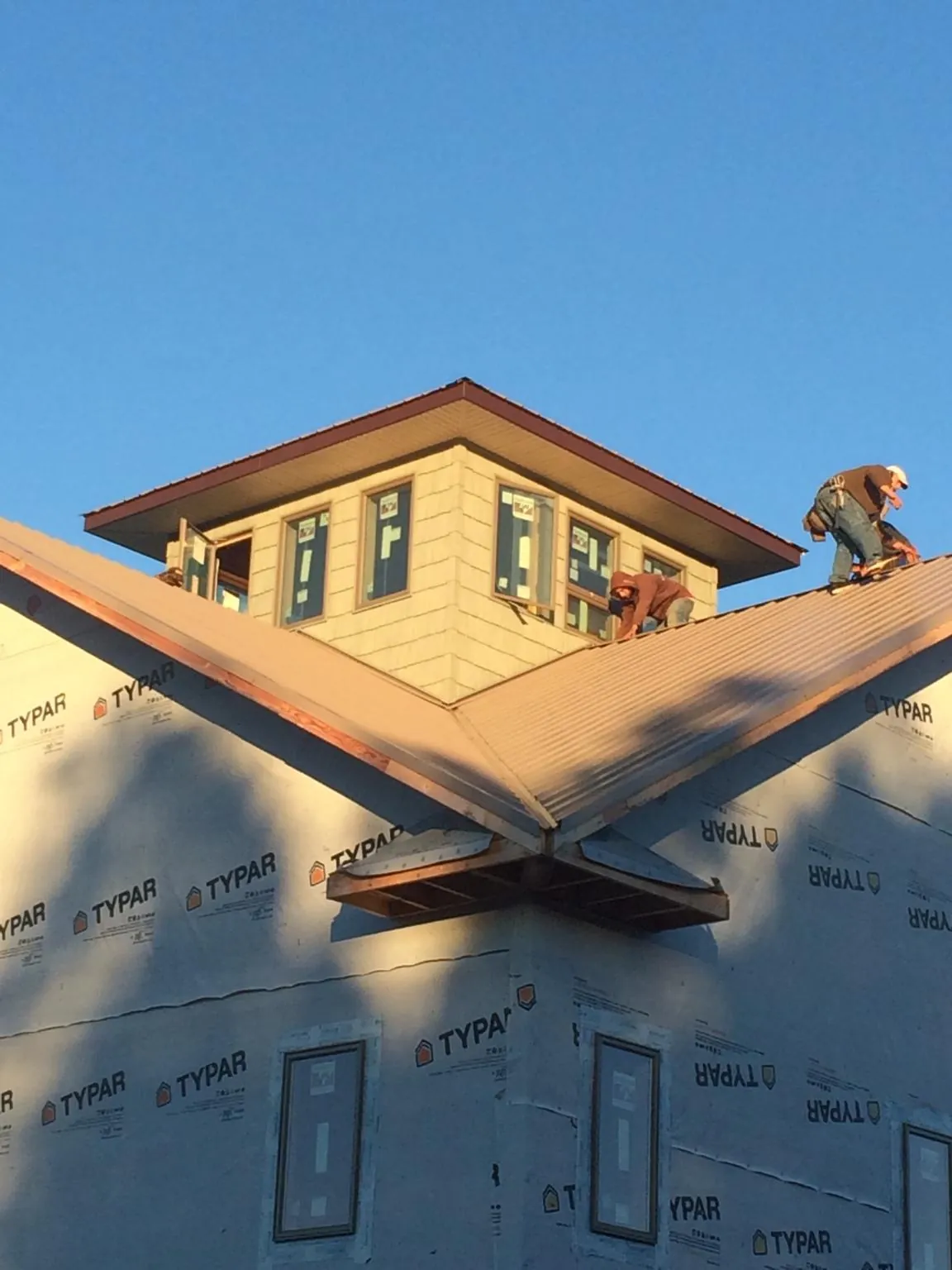 Roofers working around a rooftop cupola on a new metal roof at sunset — Roof Waterproofing in Islip Terrace by Roofing Brothers